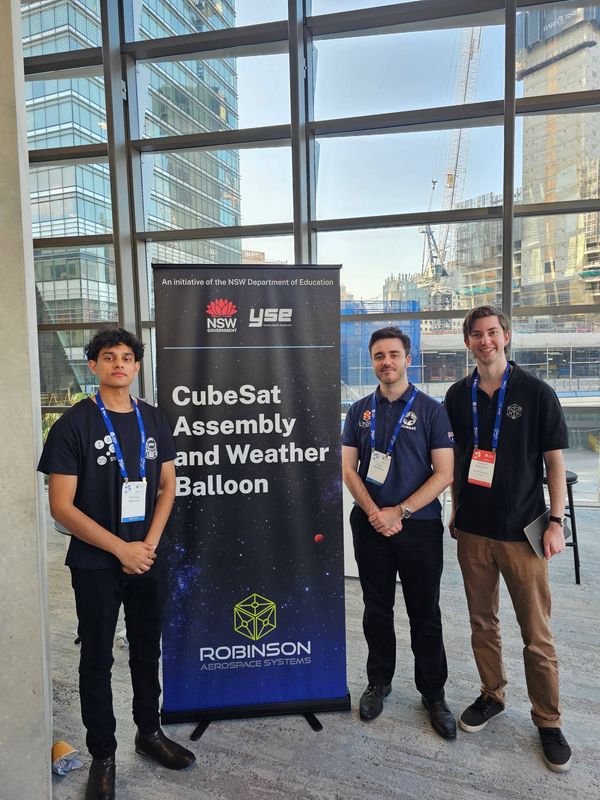 Hiranya with two workshop leads beside the CubeSat Assembly and Weather Balloon banner from Young Space Explorers and Robinson Aerospace Systems.