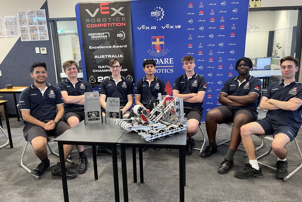 The seven person team seated around the robot and two national championship trophies.