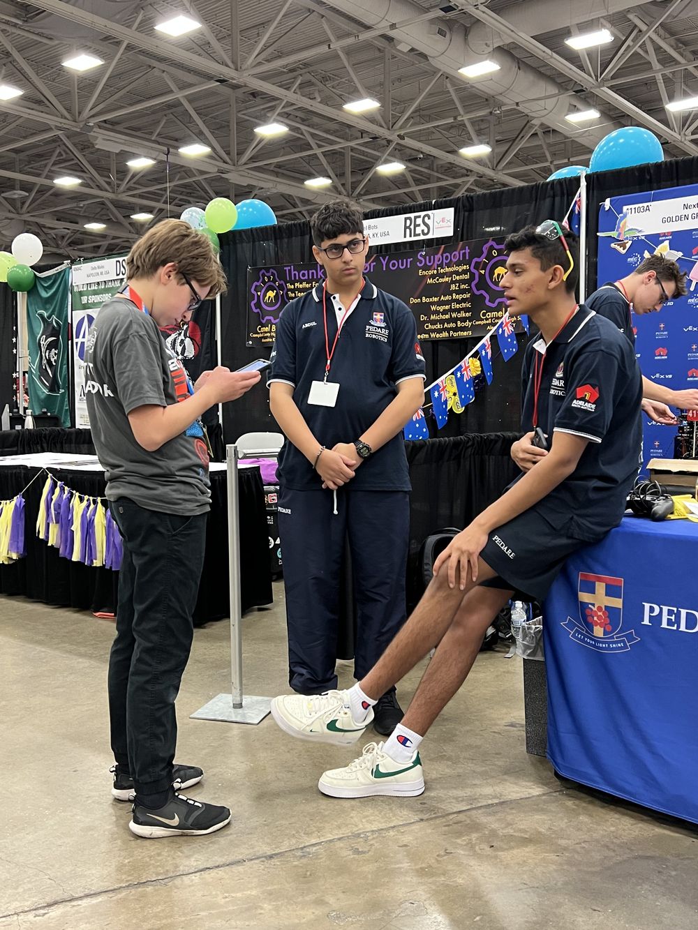 Team members in the pit area at the VEX World Championship in Dallas, standing beside the 41103A pit banner among hundreds of other team stands.