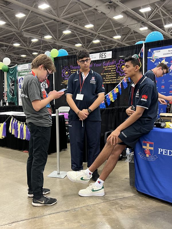 Team members in the pit area at the VEX World Championship in Dallas, beside the 41103A pit banner among hundreds of other team stands.